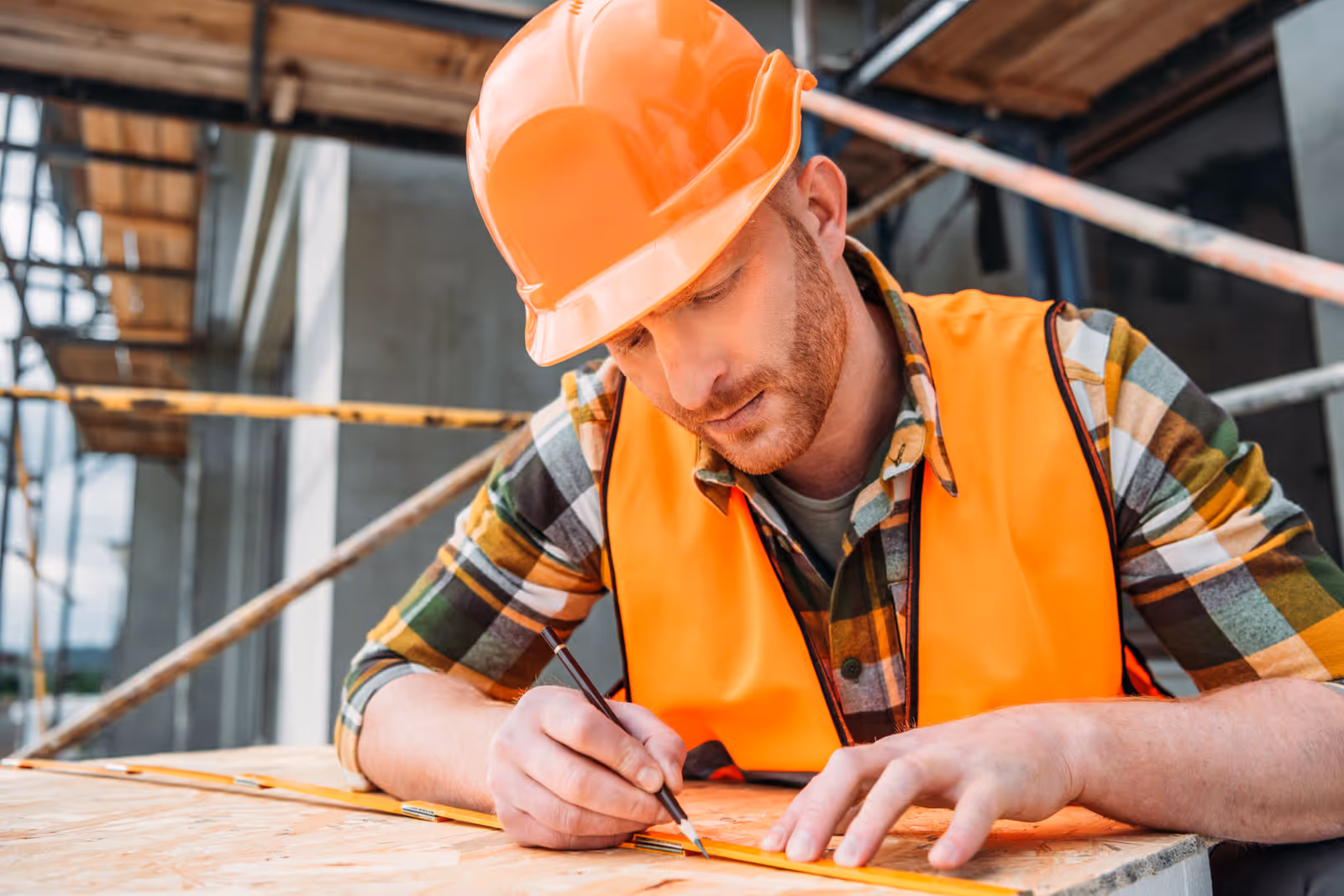Construction worker in orange hard hat measuring materials on site, representing accurate job cost tracking by category